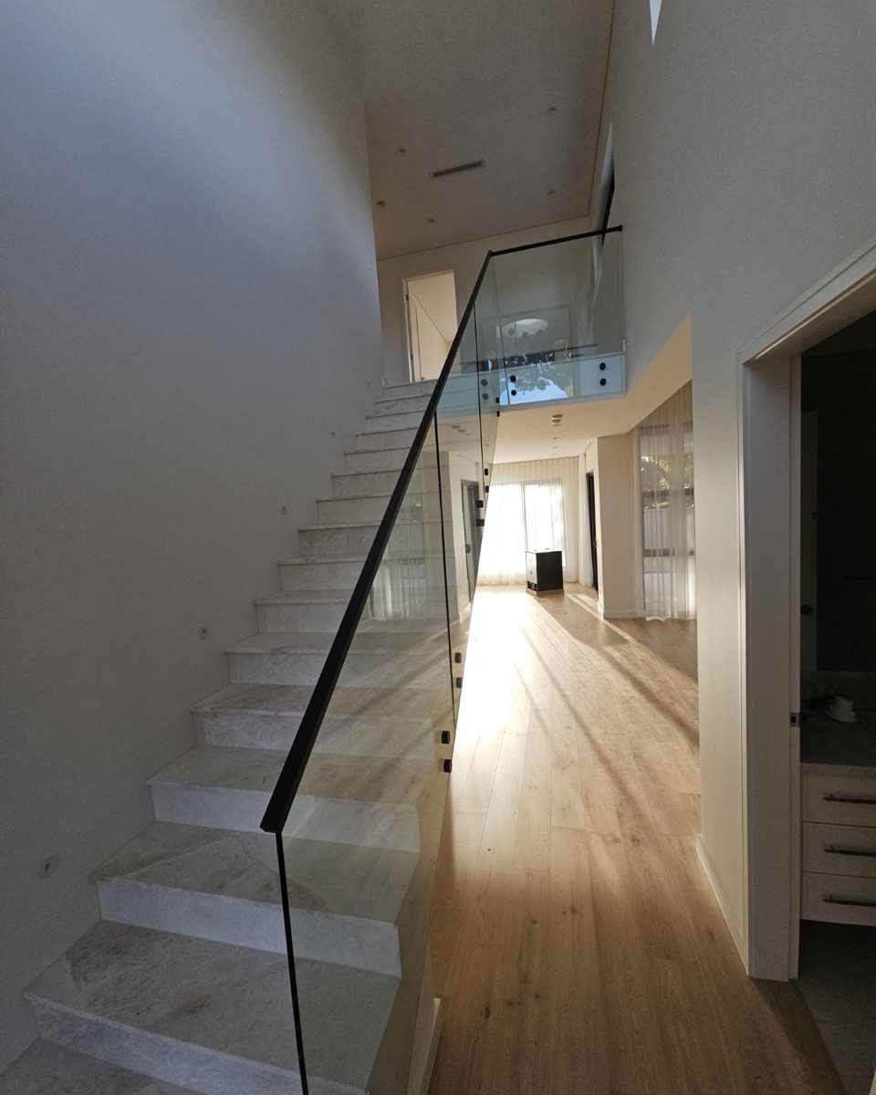 Frameless glass stair balustrade with a slim black top rail beside marble stairs