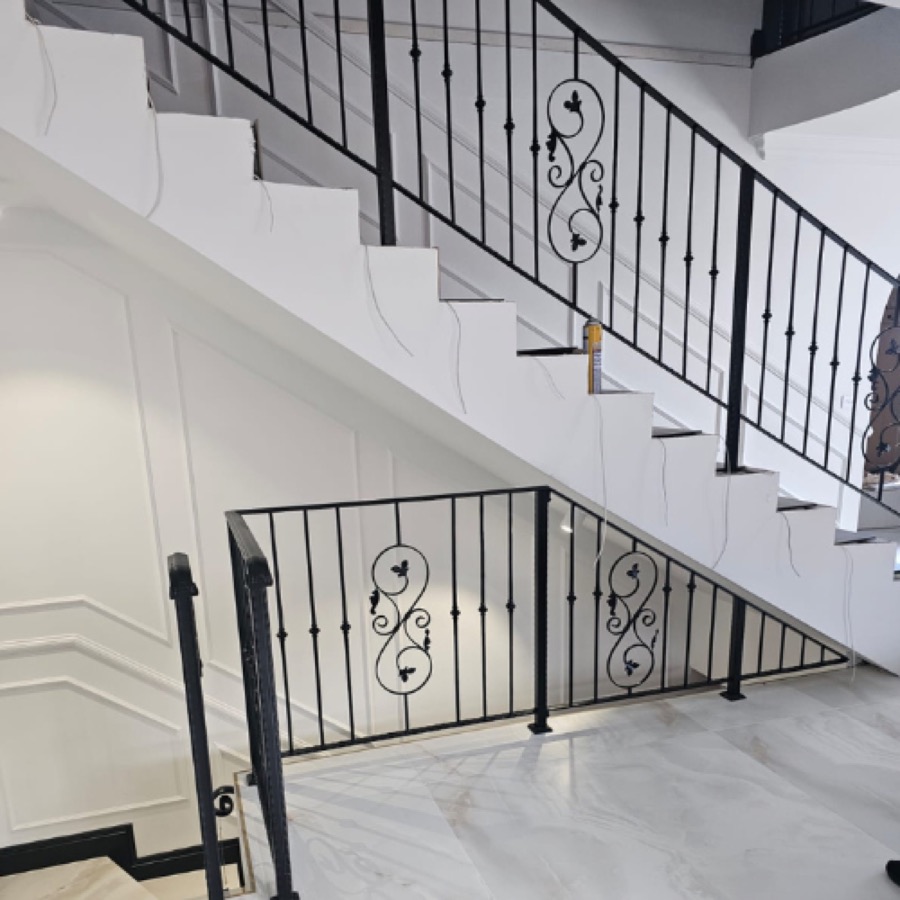 Black wrought iron balustrade with decorative scroll panels beside a white staircase