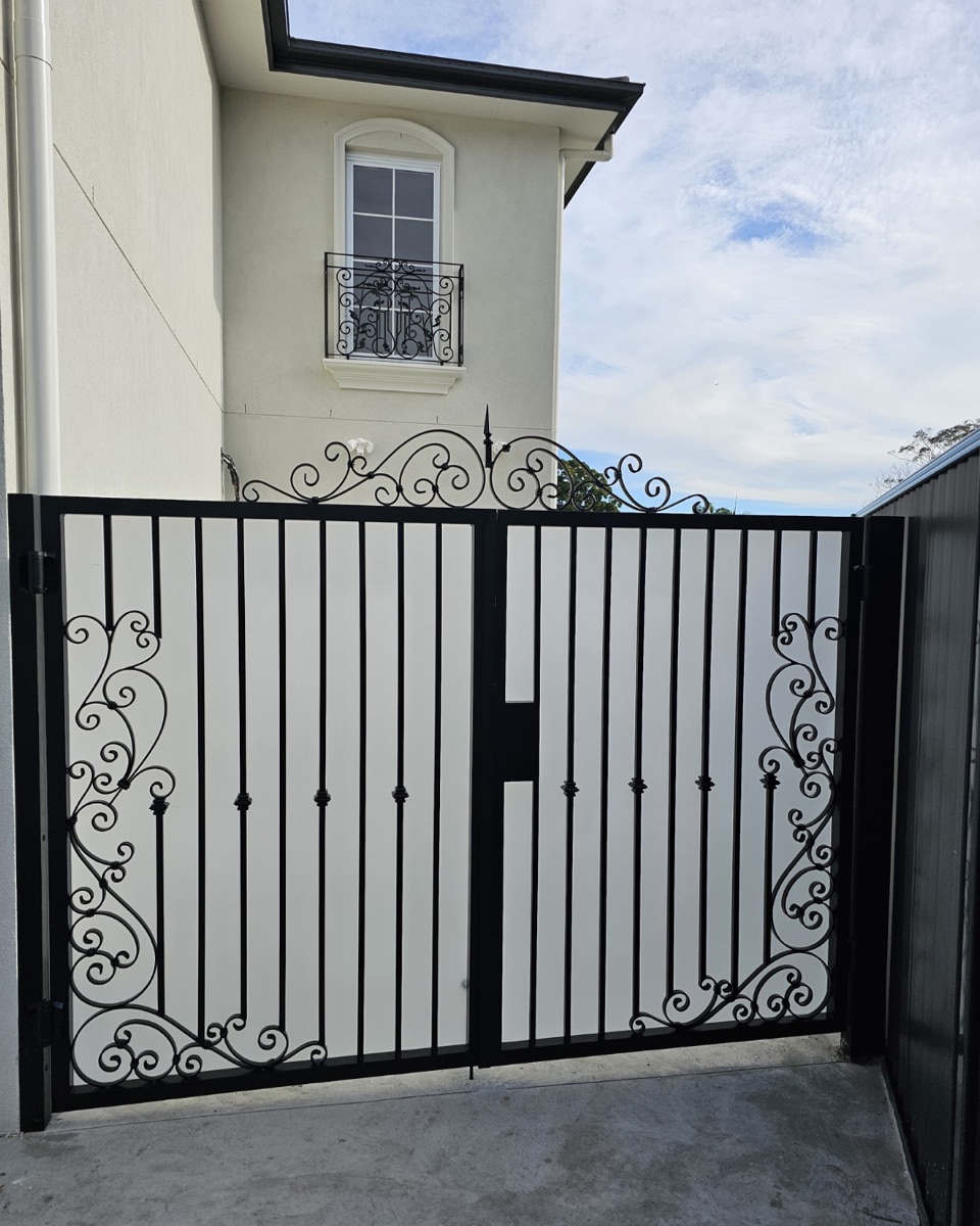 Black steel double gates with wrought iron scrollwork panels and an arched scroll topper