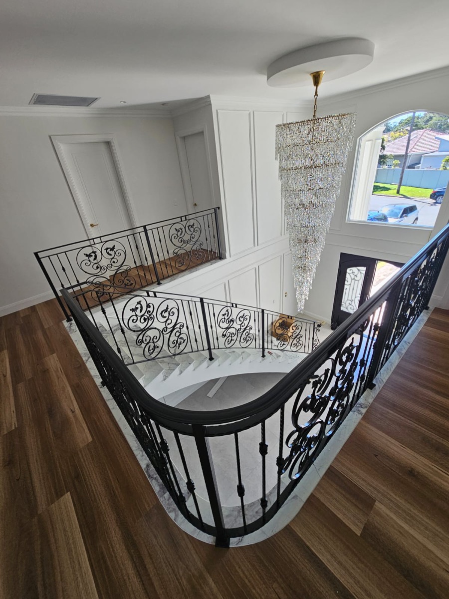Overhead view of a curved wrought iron balustrade wrapping a staircase void beneath a crystal chandelier